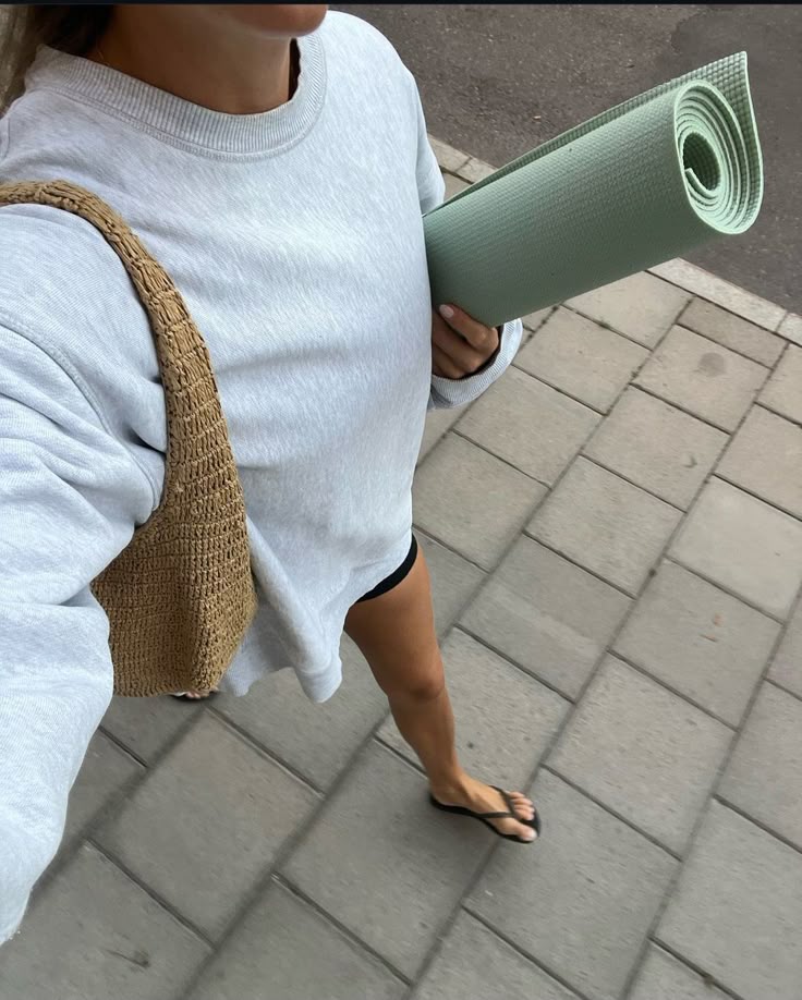 selfie of girl holding green yoga mat and tote bag walking on the sidewalk