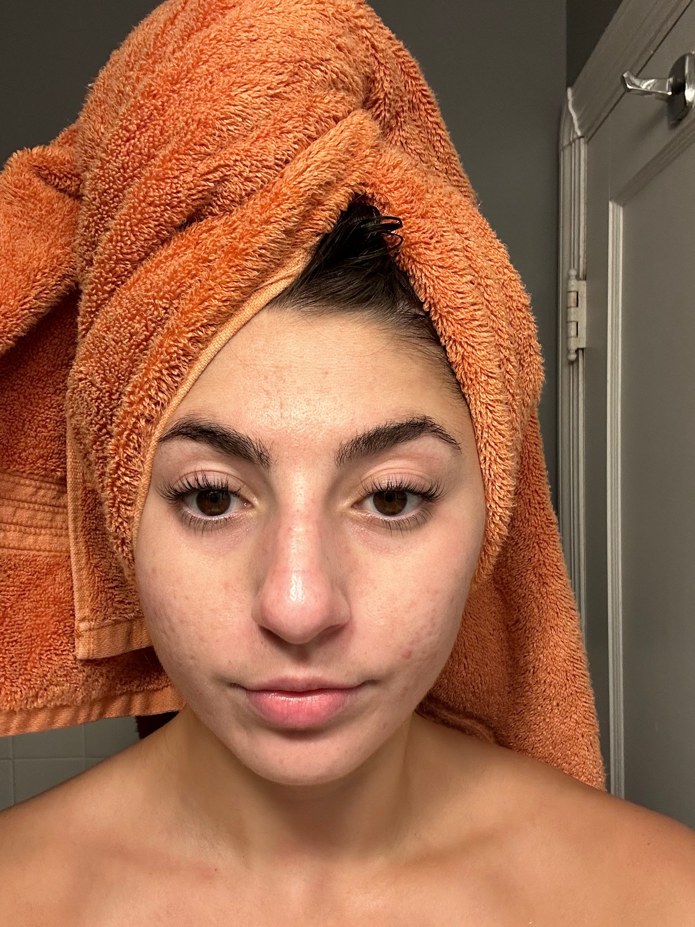 woman looking into camera in bathroom with orange towel on head